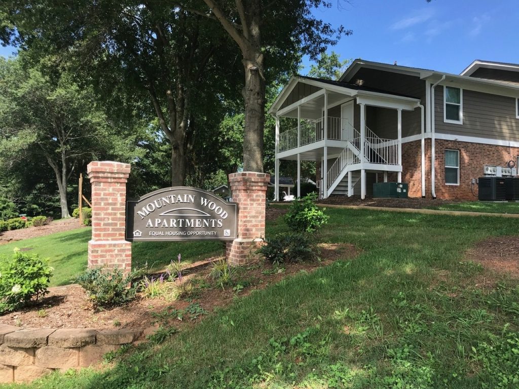 The Mountain Wood Apartments entrance monument, with a rehabbed building and new stair behind it.